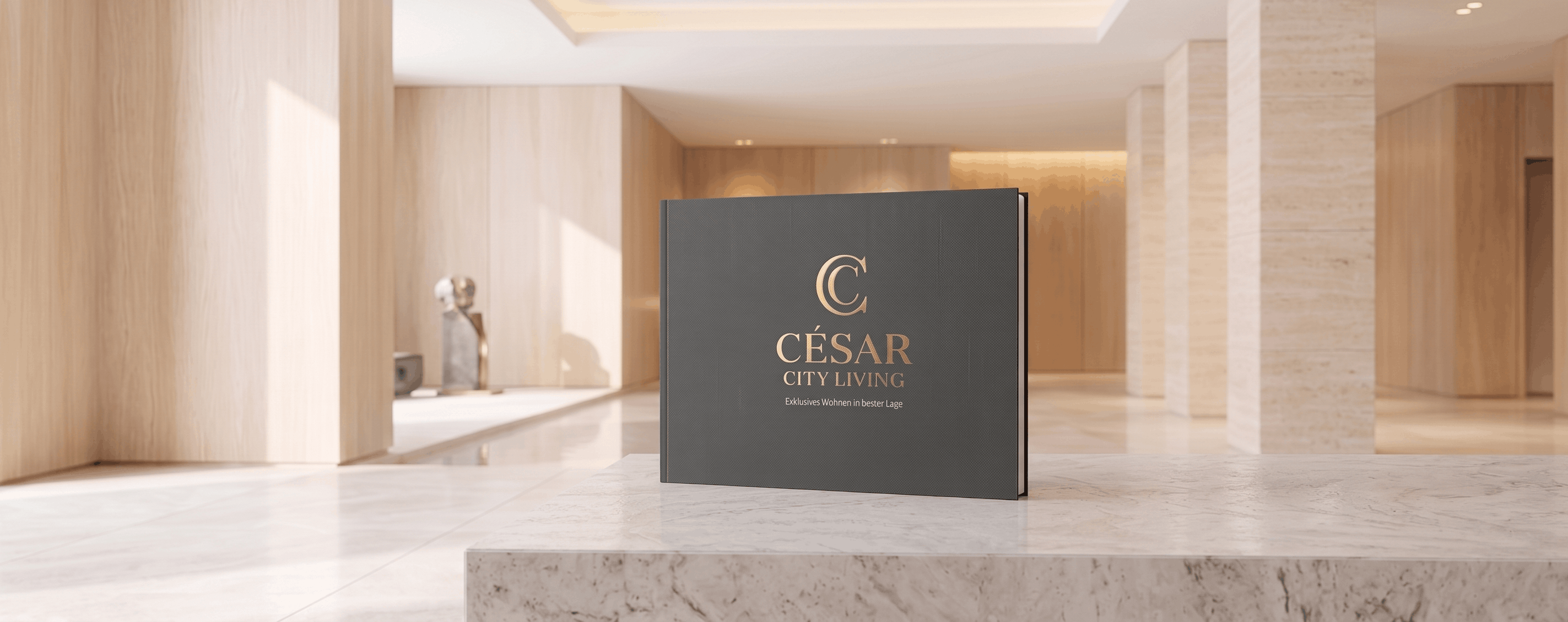 Hochwertiges Mockup eines exklusiven Immobilien-Exposés: Ein dunkelgraues Hardcover-Buch mit edler Goldprägung 'CÉSAR CITY LIVING - Exklusives Wohnen in bester Lage'. Das Buch steht auf einer hellen Marmorfläche vor dem dezent unscharfen Hintergrund eines luxuriösen, lichtdurchfluteten Foyers mit moderner Architektur